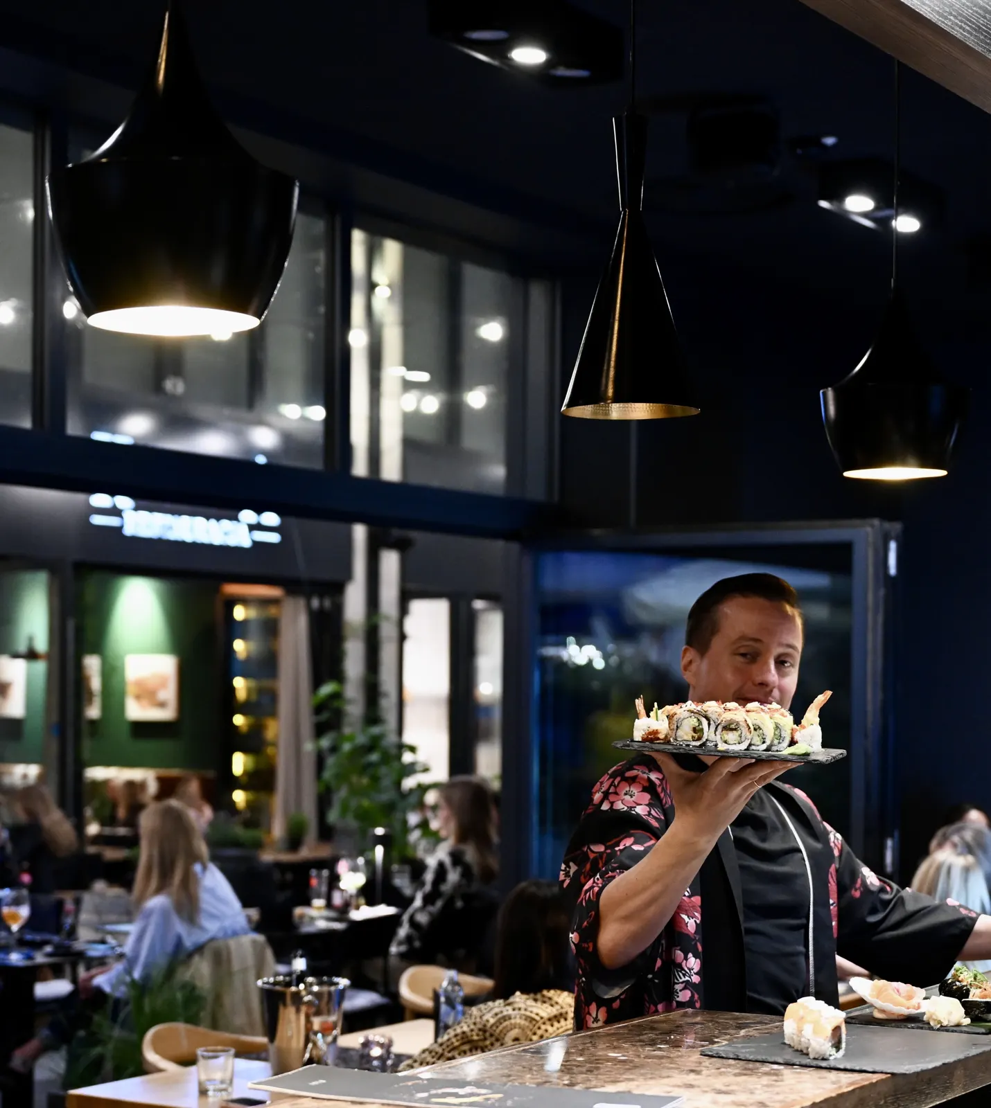 Sushi master w kimonie z rolkami sushi przy barze, w tle sala i pasaż Jatek – Bydgoszcz