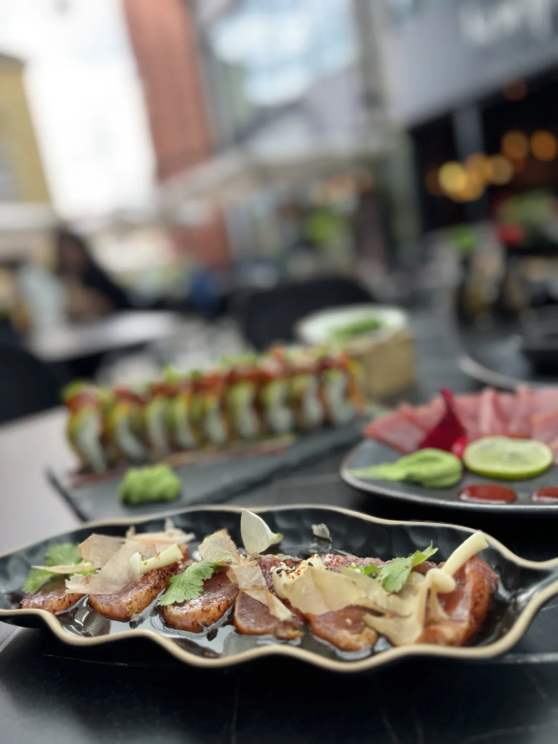 Tuna tataki – opalany tuńczyk z płatkami bonito, grzybami shimeji i sosem sezamowym z chilli, w tle rolki sushi i sashimi w ogródku King Fu Fusion – Bydgoszcz