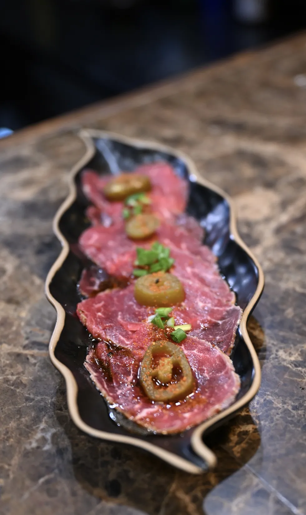 Beef tataki – opalana polędwica wołowa z jalapeño, szczypiorem i sosem black pepper na czarnym talerzu – King Fu Fusion Bydgoszcz