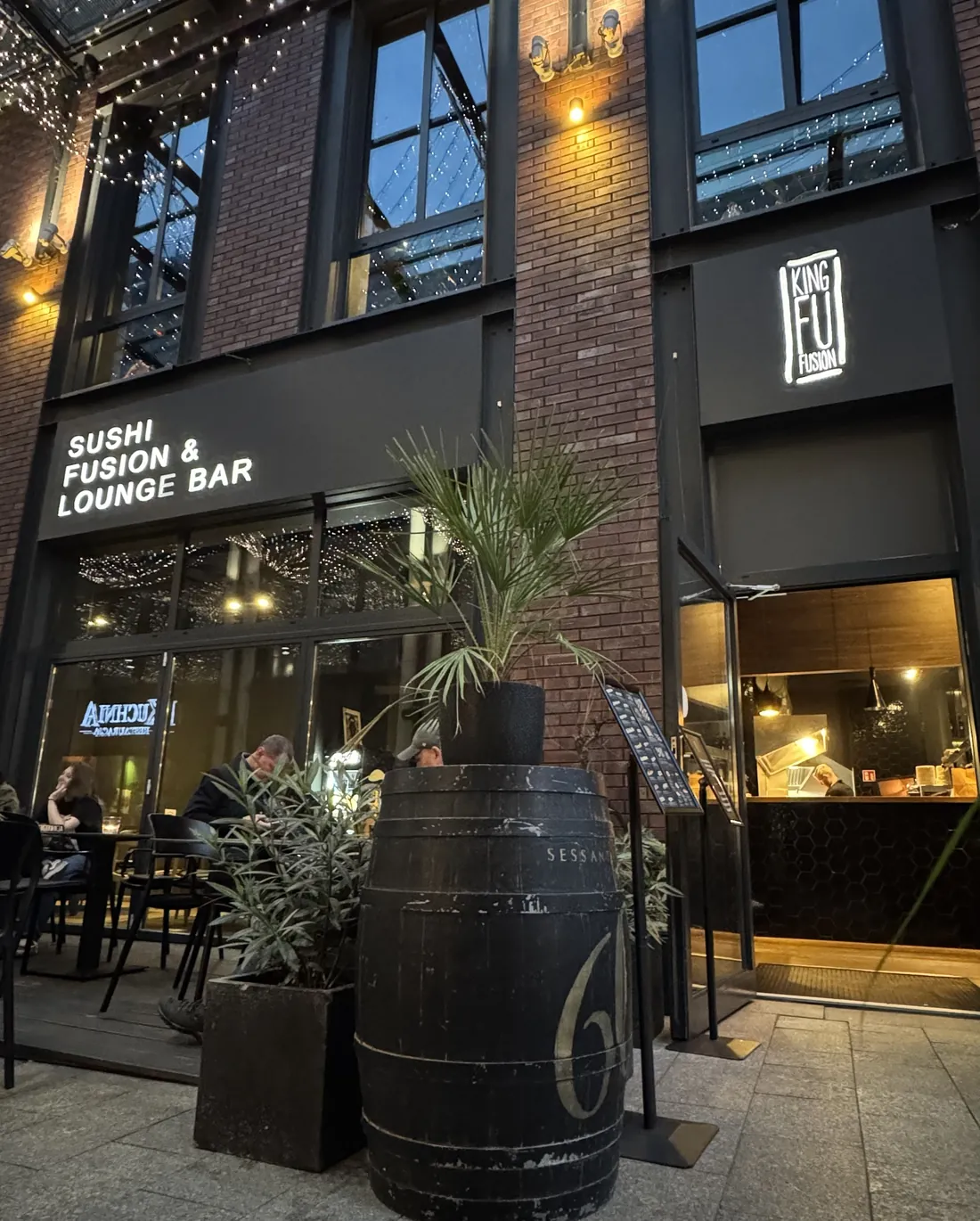 Wejście do restauracji King Fu Fusion o zmierzchu – podświetlone szyldy Sushi Fusion & Lounge Bar i logo King Fu Fusion, ogródek w pasażu Jatek w Bydgoszczy