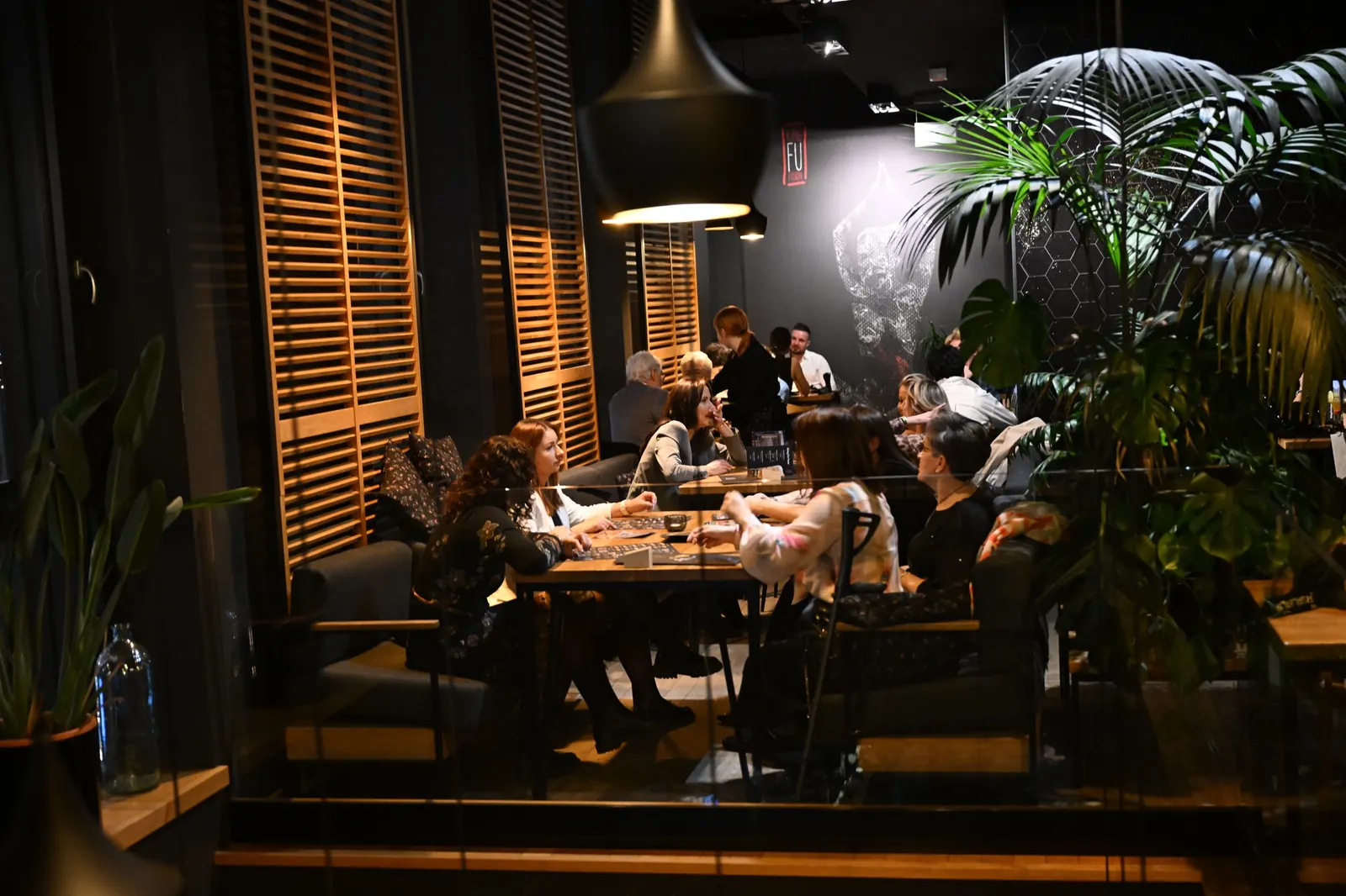 Goście przy stolikach w sali restauracji King Fu Fusion w Bydgoszczy wieczorem – drewniane okiennice, czarne lampy i palmy