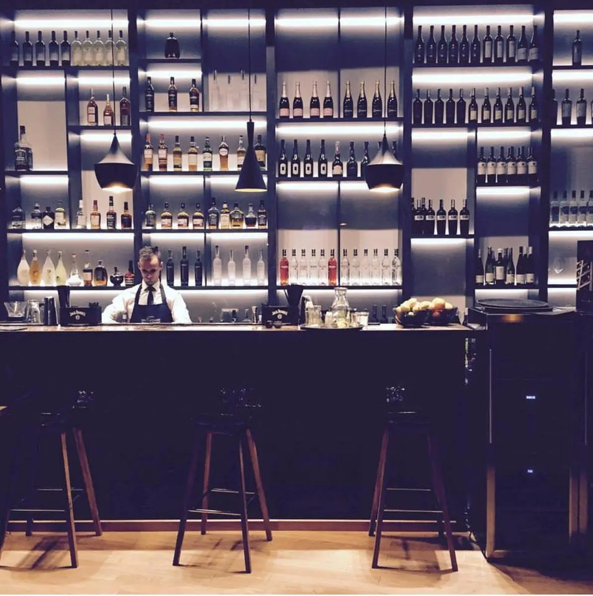 Barman za podświetlonym barem z winami i alkoholami z całego świata, czarne lampy i drewniane hokery – King Fu Fusion Bydgoszcz