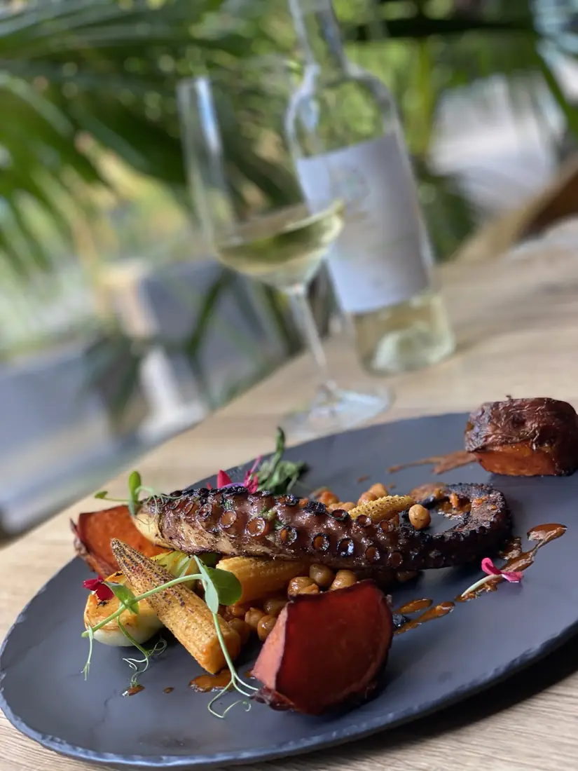 Grillowana macka ośmiornicy z ciecierzycą, pieczonym batatem i mini kukurydzą, w tle kieliszek białego wina – King Fu Fusion Bydgoszcz