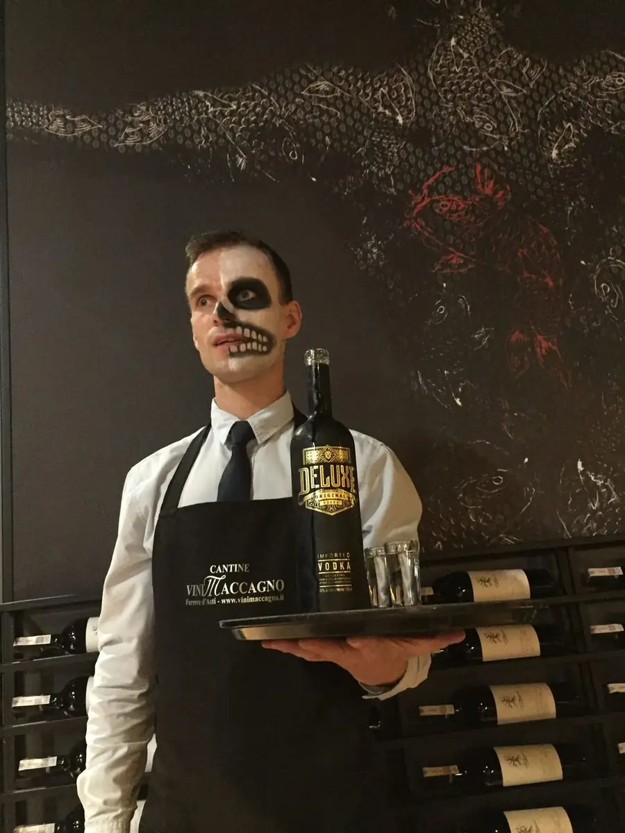 Kelner w halloweenowym makijażu czaszki podaje wódkę Deluxe na tacy na tle ściany z karpiami koi – Halloween w King Fu Fusion Bydgoszcz