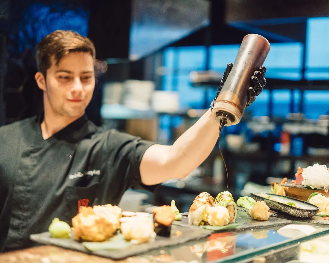 Kucharz sushi polewa sosem rolki na łupkach przy barze sushi – King Fu Fusion Bydgoszcz