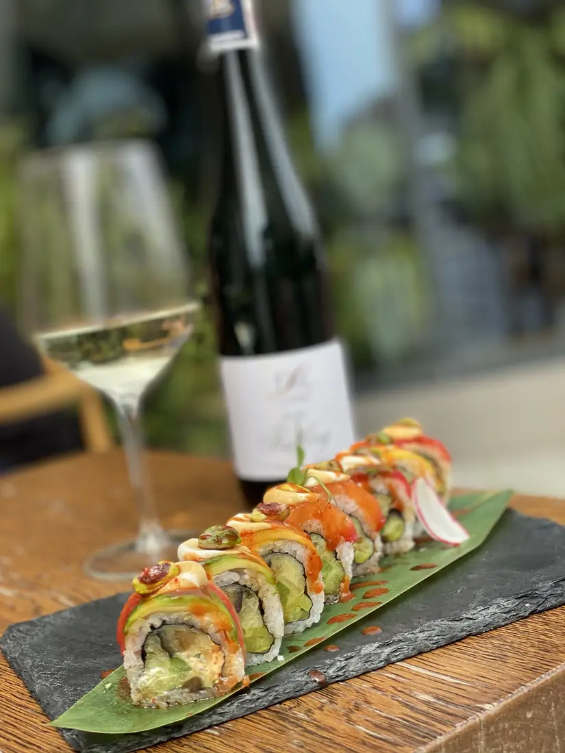 Philadelphia roll z pistacją – rolka z łososiem, tuńczykiem i awokado na łupku, w tle kieliszek i butelka Rieslinga – King Fu Fusion Bydgoszcz