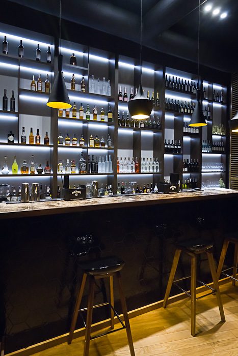 Podświetlony bar z winami i alkoholami z całego świata, czarne lampy wiszące i drewniane hokery – wnętrze King Fu Fusion Bydgoszcz