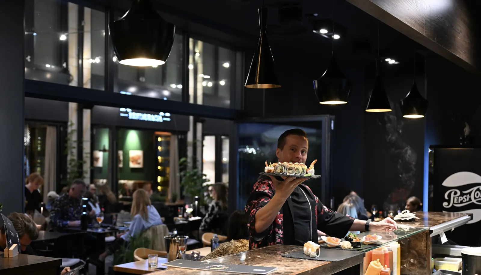 Sushi master w kimonie podaje talerz autorskich rolek przy barze sushi King Fu Fusion – Bydgoszcz