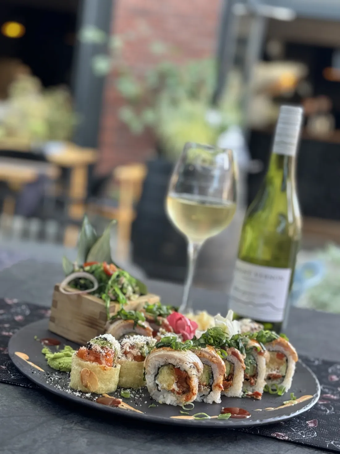Talerz autorskich rolek sushi fusion – rolki w tempurze i migdałach, opalany łosoś, sałatka wakame – z kieliszkiem i butelką Mount Vernon Sauvignon Blanc z Nowej Zelandii w ogródku King Fu Fusion – Bydgoszcz