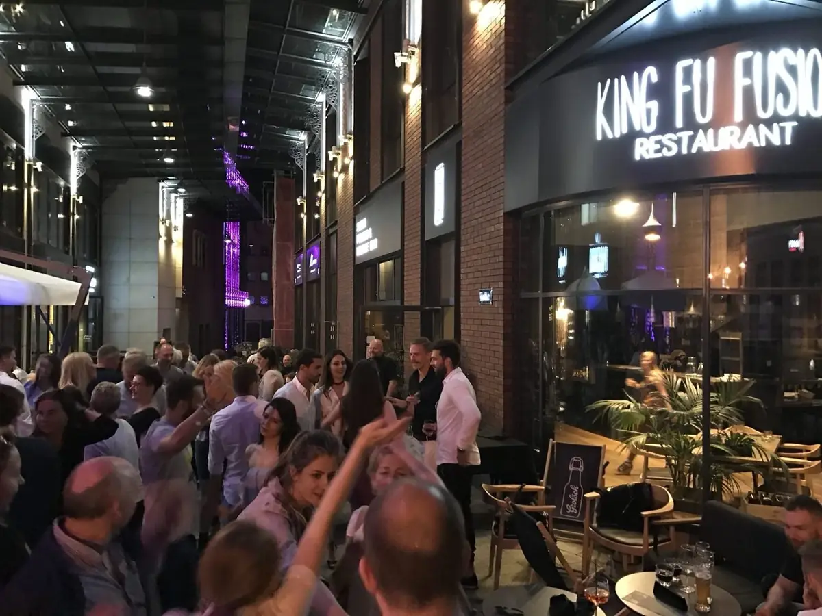 Tłum bawiących się gości przed restauracją King Fu Fusion w pasażu Jatki wieczorem – podświetlony szyld i ogródek, Bydgoszcz