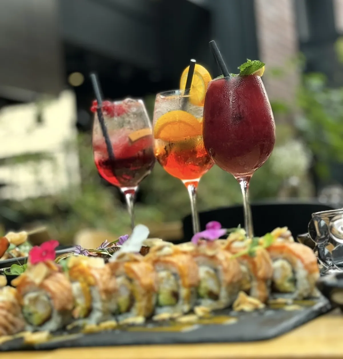 Trzy kolorowe koktajle z owocami i miętą oraz autorska rolka sushi fusion z opalanym łososiem i jadalnymi kwiatami w ogródku King Fu Fusion – Bydgoszcz